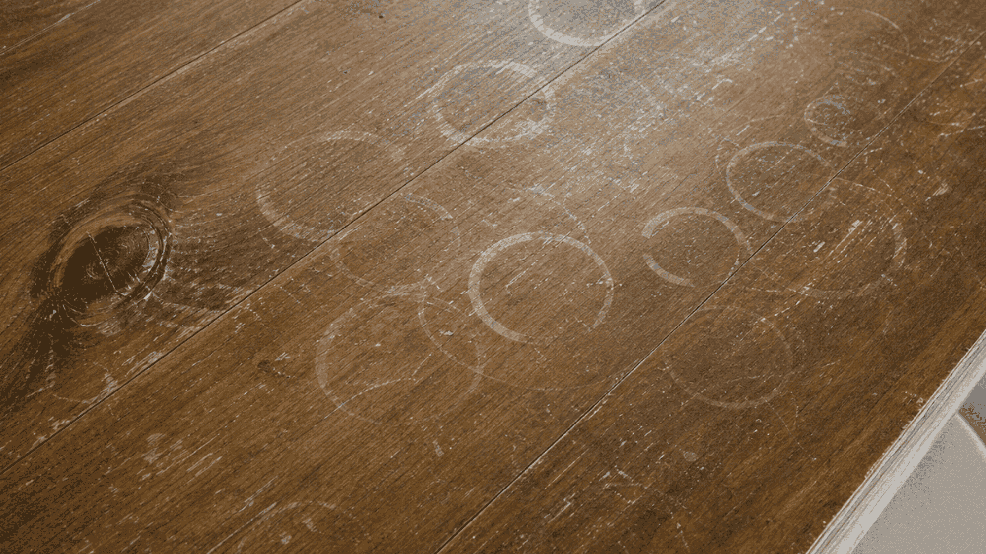 White water rings and stains visible across a dark wooden tabletop from cups and moisture damage