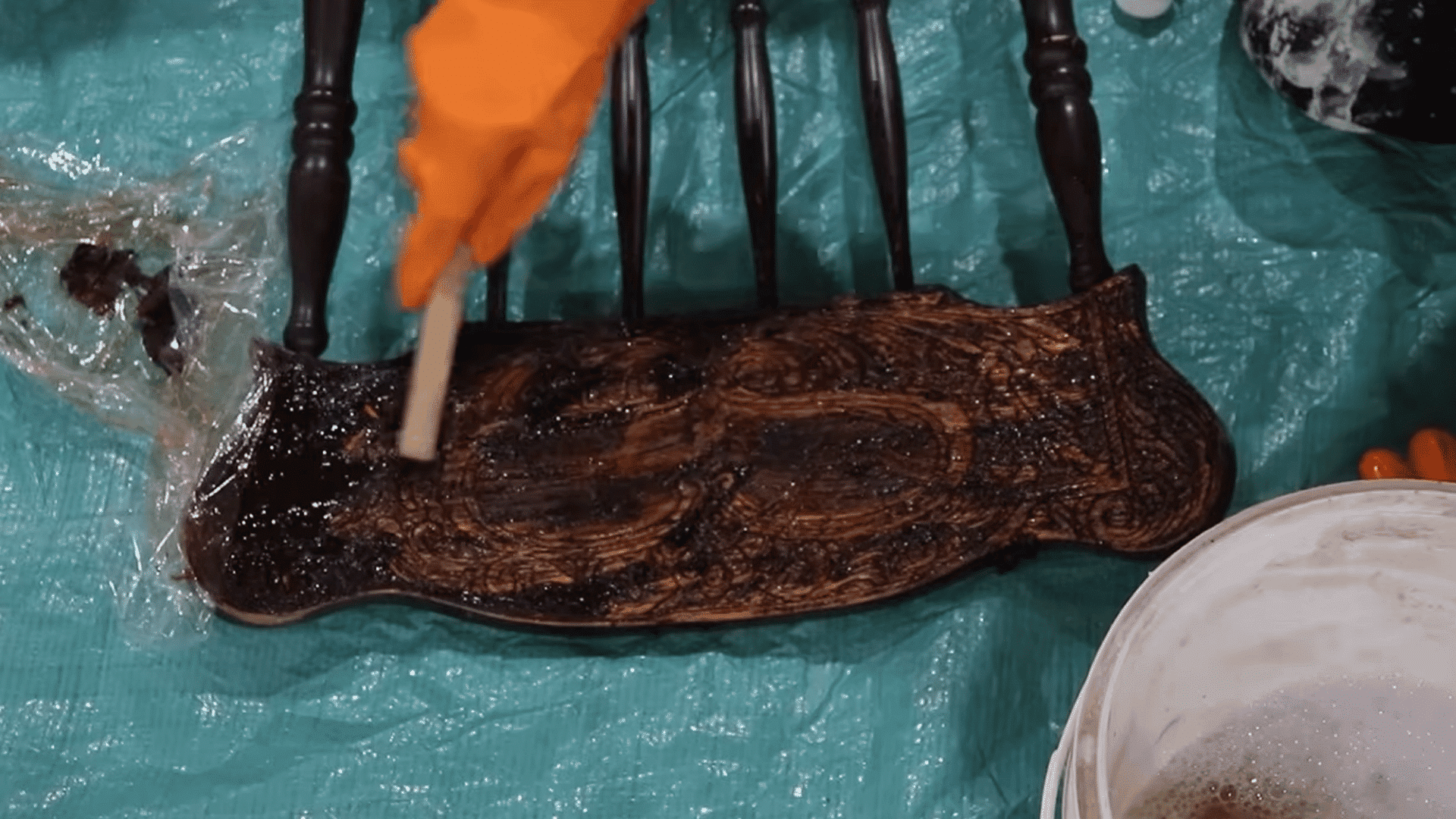 Using a wire brush to remove softened paint from carved wooden furniture details
